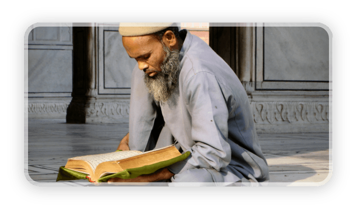 Mężczyzna z długą brodą siedzi po turecku i czyta książkę